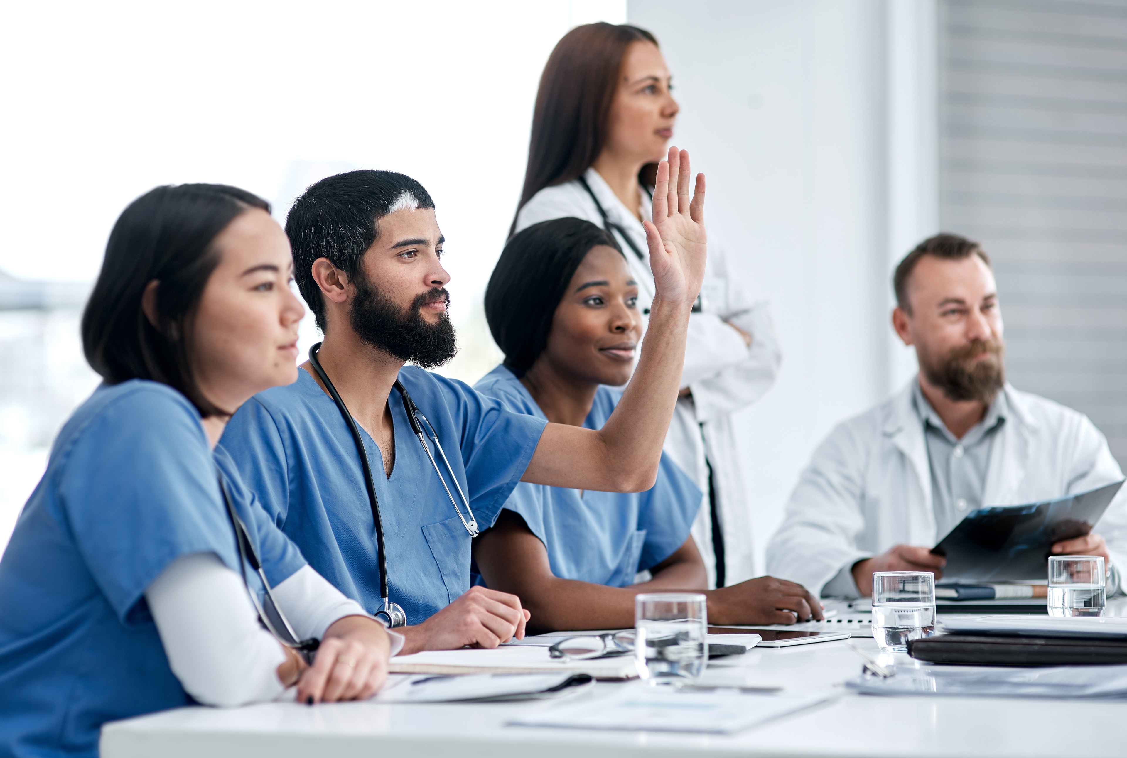 About Us – Nursing Leadership Certification Healthcare professionals in a meeting with a doctor raising his hand to participate